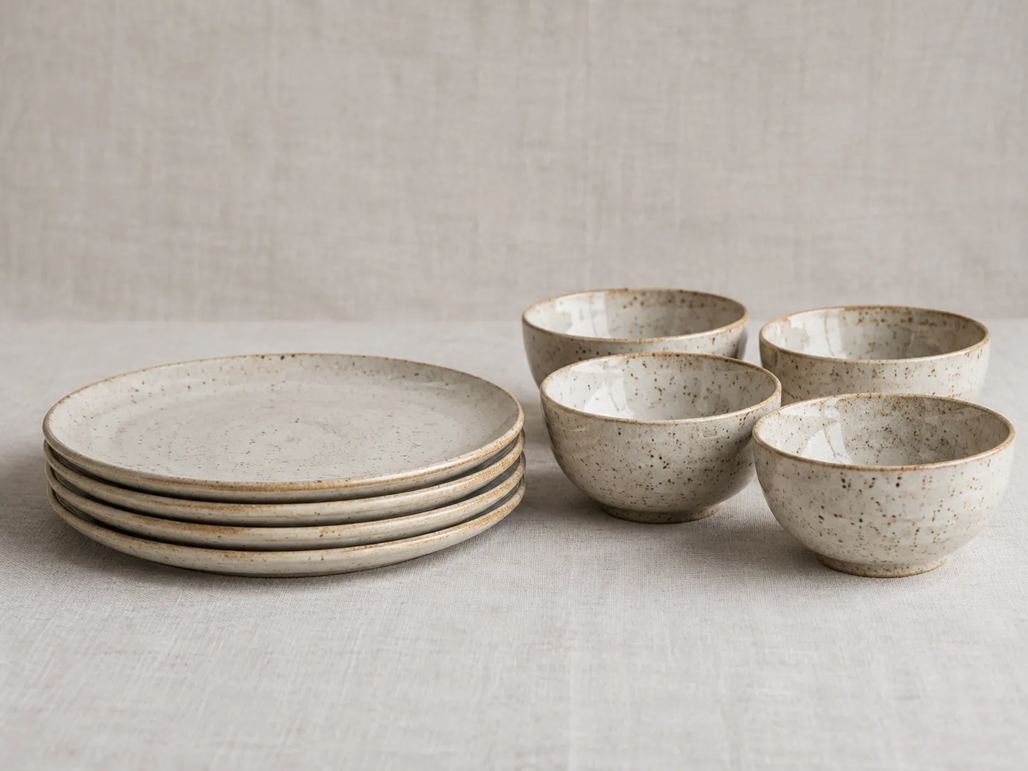 Four speckled oatmeal plates stacked beside four matching bowls.