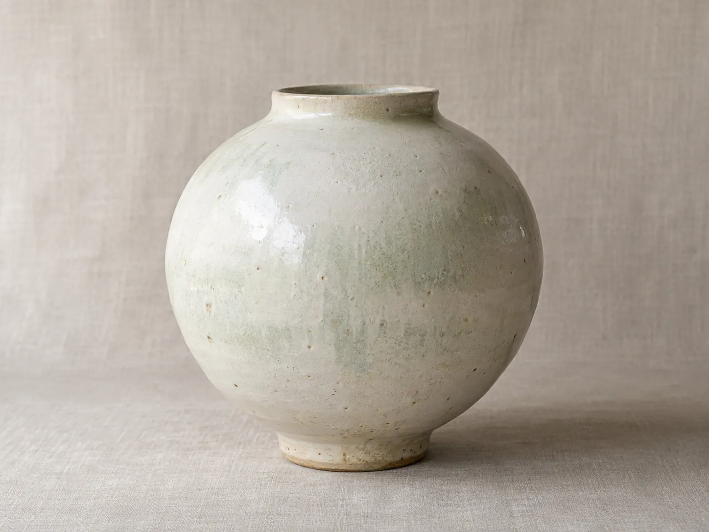 A large round white moon jar with a pale green blush.